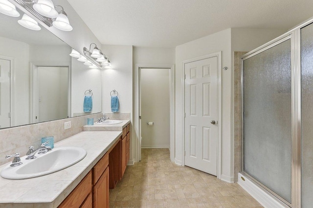 full bathroom with double vanity, baseboards, a shower stall, and a sink