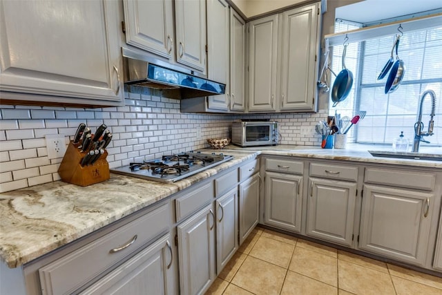 kitchen featuring stainless steel gas cooktop, light tile patterned flooring, gray cabinets, under cabinet range hood, and a sink