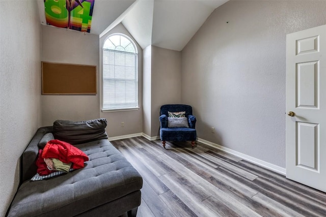 living area featuring baseboards, vaulted ceiling, a textured wall, and wood finished floors