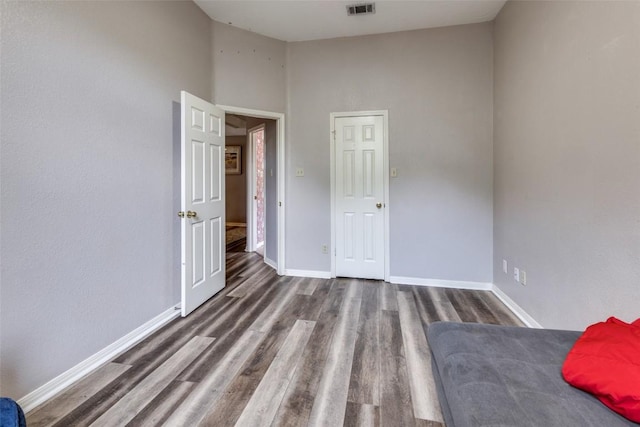 unfurnished bedroom with baseboards, a towering ceiling, wood finished floors, and visible vents