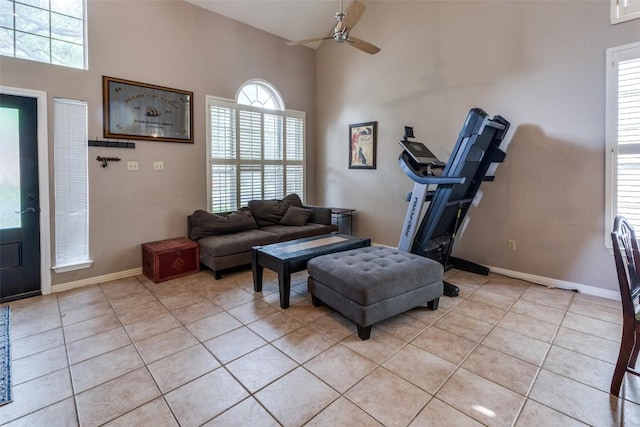 living room featuring baseboards, a ceiling fan, a high ceiling, and light tile patterned floors