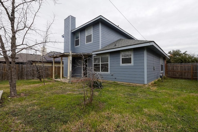 rear view of house featuring a fenced backyard, a yard, and a chimney