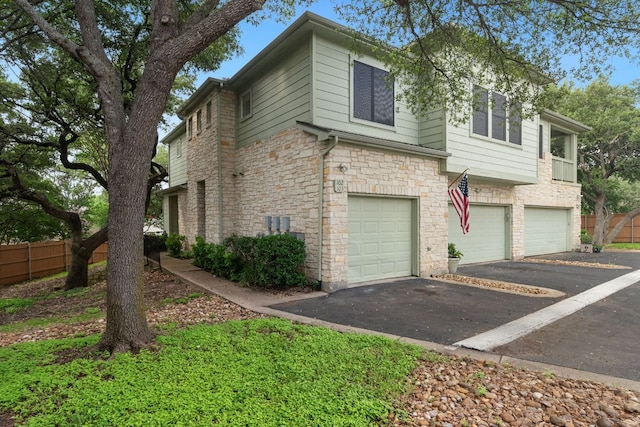 view of home's exterior with fence, an attached garage, driveway, and stone siding