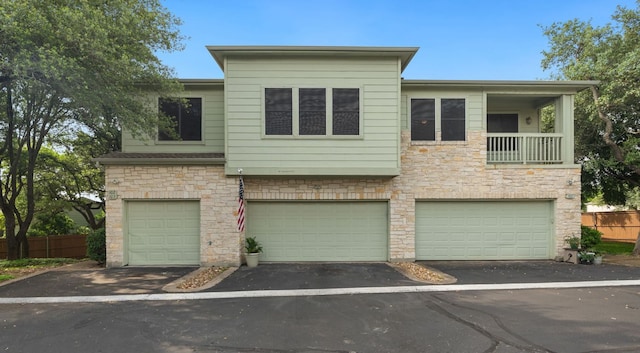 view of property featuring fence, an attached garage, driveway, and stone siding