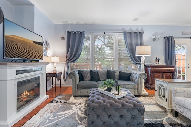 living room with crown molding, baseboards, a glass covered fireplace, and wood finished floors