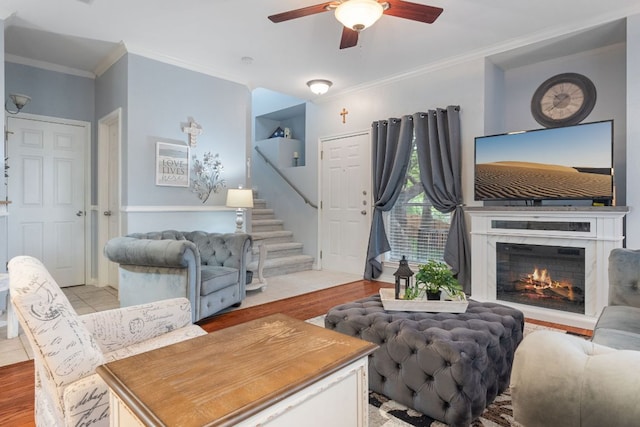 living area with stairs, a ceiling fan, crown molding, and light wood-style flooring