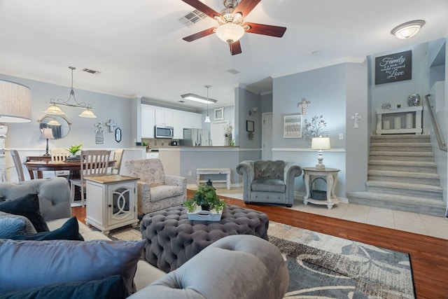 living room with ceiling fan, ornamental molding, light wood finished floors, and visible vents