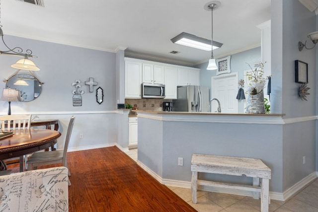 kitchen with decorative backsplash, pendant lighting, white cabinets, ornamental molding, and stainless steel appliances