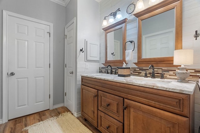 full bath featuring double vanity, decorative backsplash, crown molding, wood finished floors, and a sink