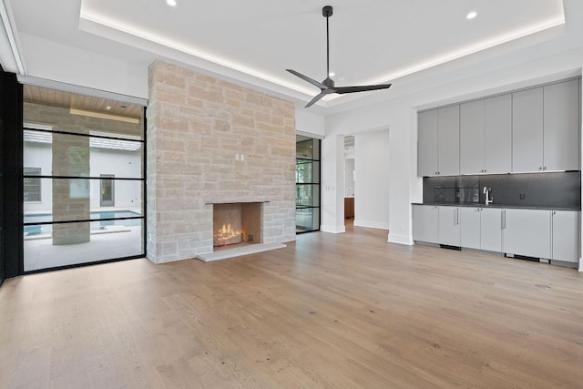 229 Tiffanie Way, Austin, TX 78737 - unfurnished living room featuring a ceiling fan, a stone fireplace, a tray ceiling, recessed lighting, and light wood-style flooring