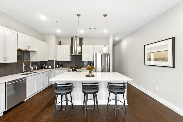 kitchen with a kitchen island, wall chimney range hood, a kitchen bar, a sink, and appliances with stainless steel finishes