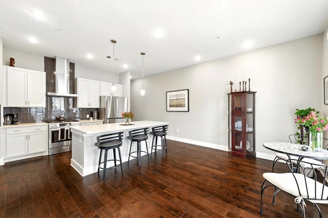 kitchen with a kitchen island, appliances with stainless steel finishes, light countertops, a breakfast bar, and wall chimney exhaust hood