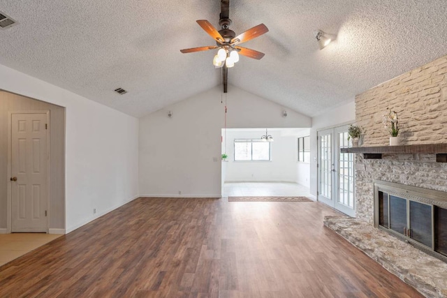 unfurnished living room featuring ceiling fan, a textured ceiling, visible vents, a fireplace, and wood finished floors