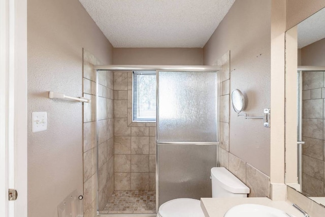 bathroom with vanity, toilet, a textured ceiling, and a stall shower