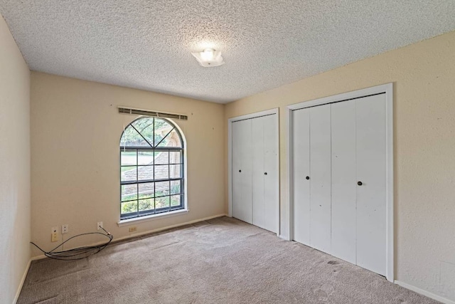 unfurnished bedroom with two closets, a textured ceiling, carpet floors, and baseboards