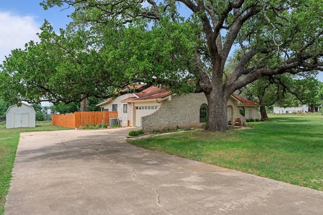 view of front facade with fence, cooling unit, a front lawn, a storage unit, and stone siding