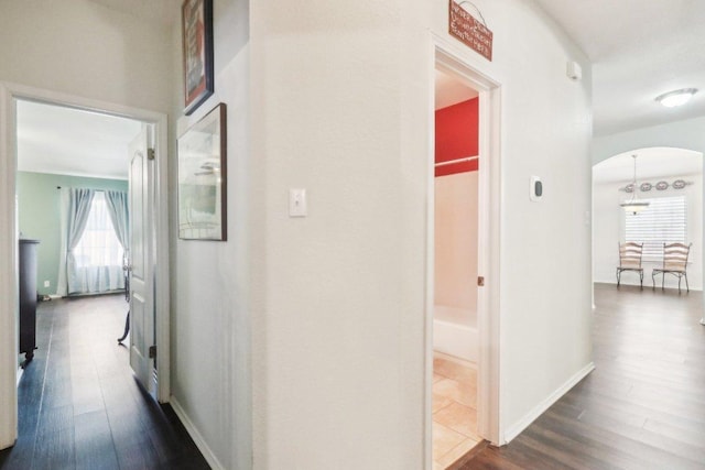 hallway with arched walkways, baseboards, and dark wood finished floors