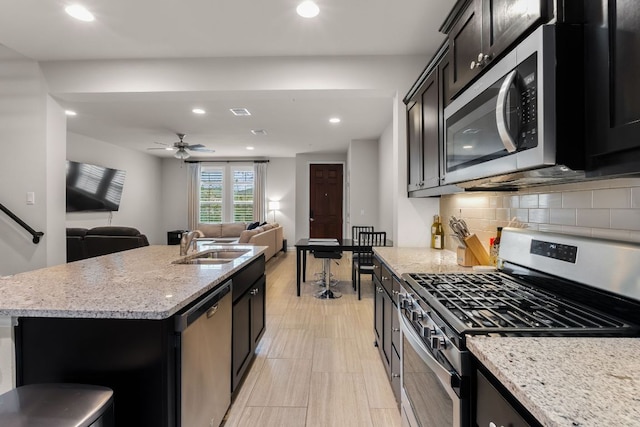 kitchen with decorative backsplash, a sink, light stone counters, open floor plan, and stainless steel appliances
