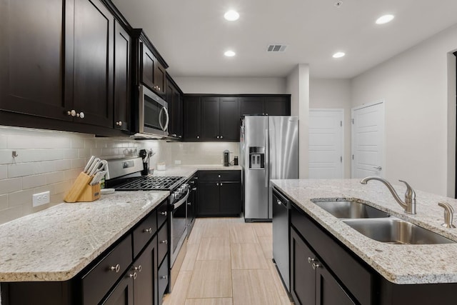 kitchen with a kitchen island with sink, tasteful backsplash, a sink, stainless steel appliances, and recessed lighting