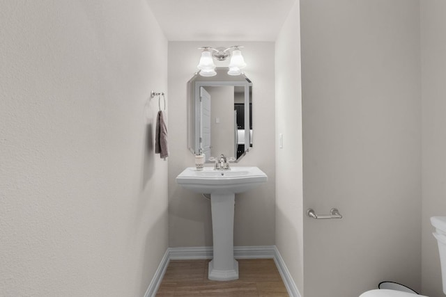 half bath with toilet, baseboards, and wood finished floors
