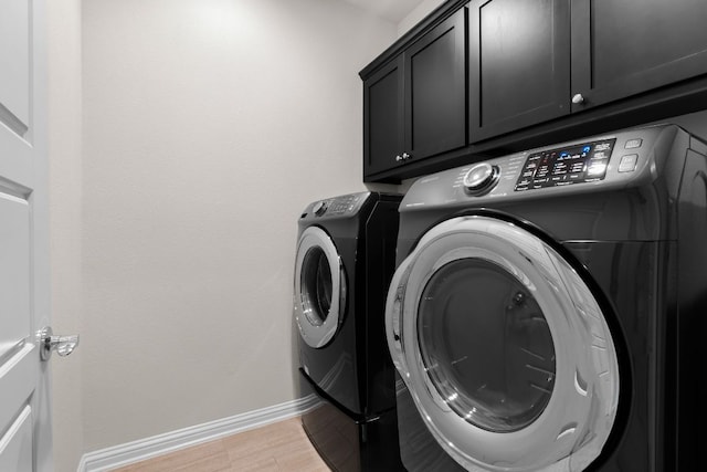 laundry area featuring cabinet space, baseboards, washer and clothes dryer, and light wood finished floors
