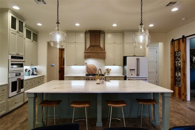 kitchen featuring visible vents, white appliances, dark wood-style floors, a barn door, and custom range hood