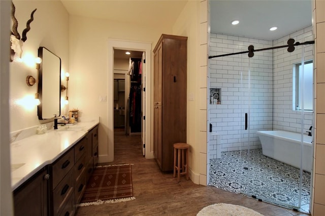 bathroom with double vanity, wood finished floors, recessed lighting, a freestanding bath, and a stall shower