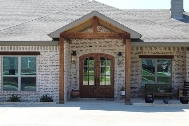 entrance to property with brick siding, a shingled roof, french doors, and a chimney