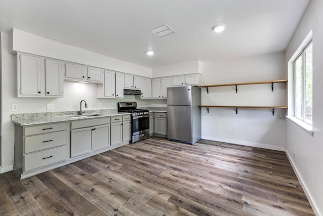 kitchen with dark wood-style floors, under cabinet range hood, a sink, appliances with stainless steel finishes, and gray cabinetry