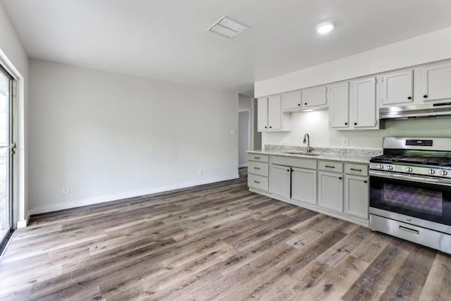 5912 Wagon Bnd, Austin, TX 78744 - kitchen with stainless steel range with gas stovetop, under cabinet range hood, wood finished floors, light stone counters, and gray cabinets