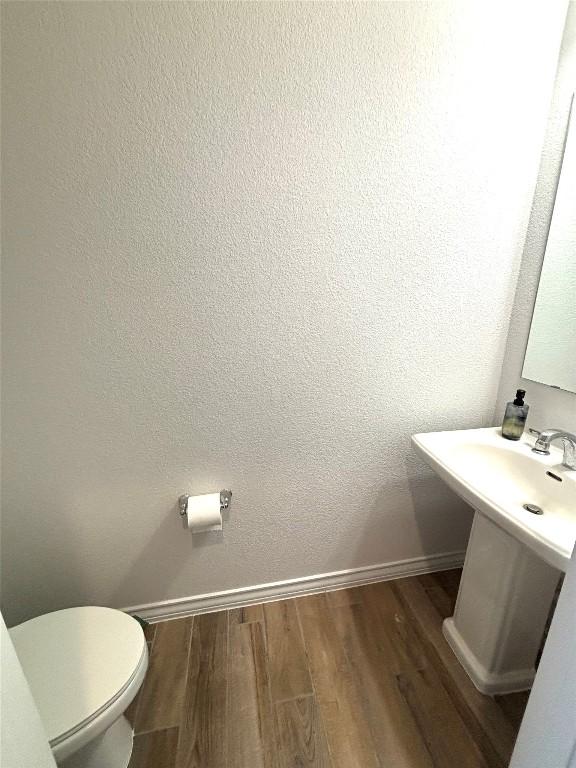half bathroom with baseboards, wood finished floors, and toilet