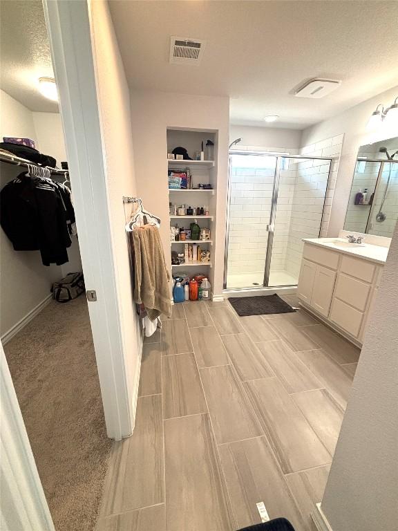 full bath featuring vanity, a walk in closet, a stall shower, and visible vents