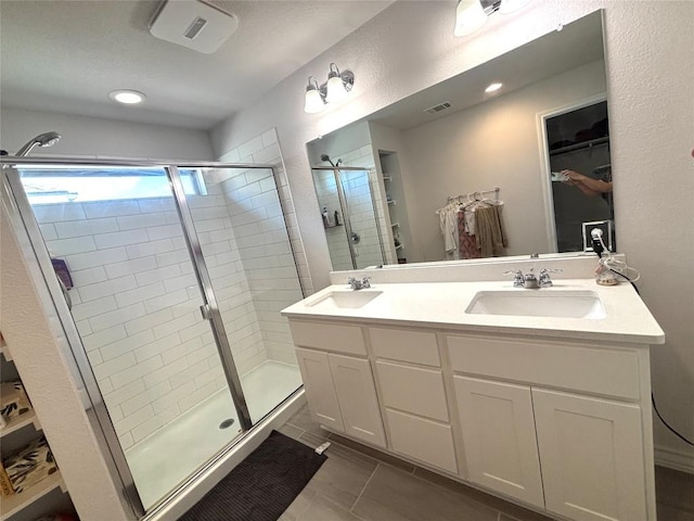 full bath with double vanity, a walk in closet, a sink, and a stall shower