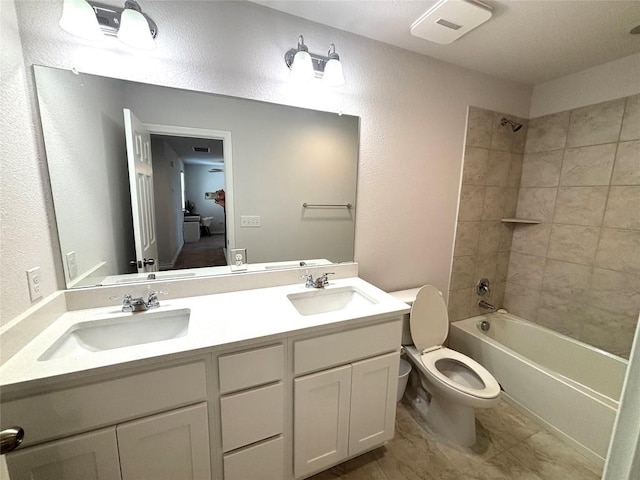 full bath featuring double vanity, toilet, a textured wall, and a sink