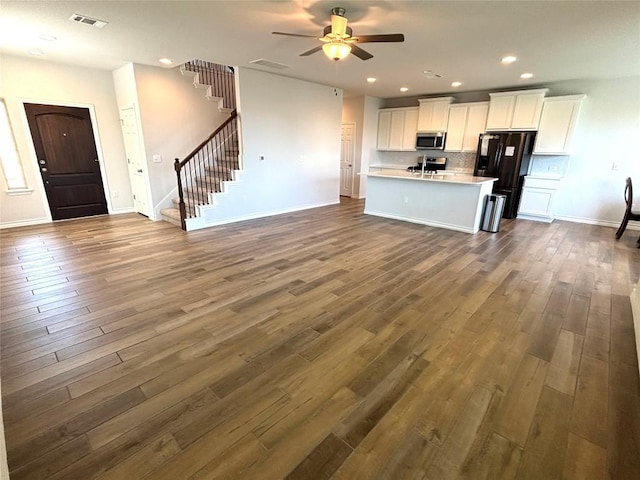 kitchen with dark wood-style flooring, black refrigerator with ice dispenser, stainless steel microwave, open floor plan, and visible vents