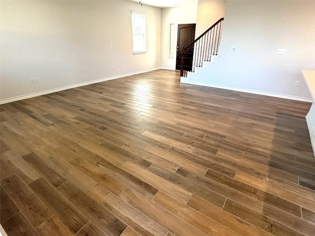 unfurnished living room with stairway, baseboards, and dark wood-style floors