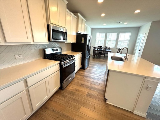 kitchen with appliances with stainless steel finishes, a sink, a kitchen island with sink, recessed lighting, and wood finished floors