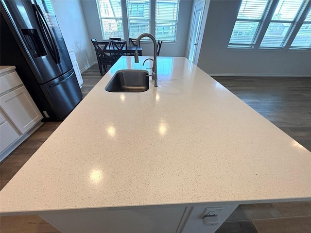 kitchen featuring black fridge, a sink, white cabinetry, baseboards, and a large island with sink