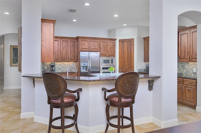kitchen featuring dark stone counters, appliances with stainless steel finishes, a peninsula, and arched walkways