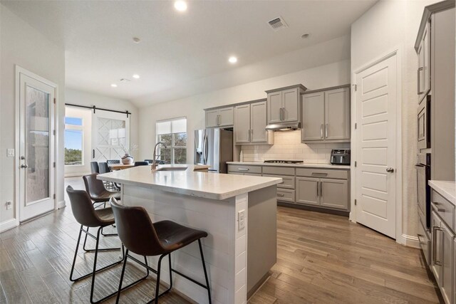 216 Vista Village Cv, Austin, TX 78738 - kitchen with gray cabinetry, stainless steel appliances, a breakfast bar area, wood finished floors, and recessed lighting