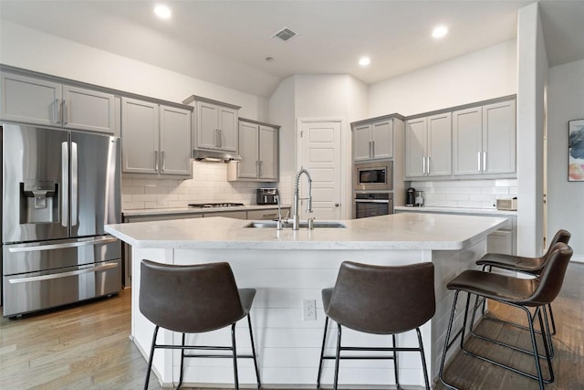 216 Vista Village Cv, Austin, TX 78738 - kitchen featuring appliances with stainless steel finishes, gray cabinets, backsplash, a breakfast bar, and light wood finished floors