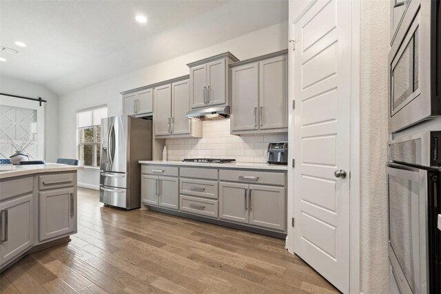 216 Vista Village Cv, Austin, TX 78738 - kitchen featuring gray cabinets, stainless steel appliances, light countertops, decorative backsplash, and lofted ceiling