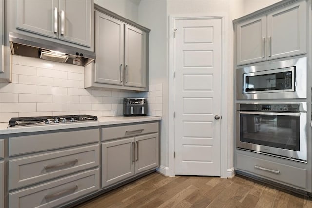 216 Vista Village Cv, Austin, TX 78738 - kitchen with stainless steel appliances, gray cabinets, under cabinet range hood, dark wood-style floors, and light countertops