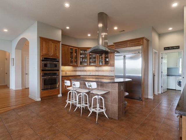 19200 White Horse Cv, Spicewood, TX 78669 - kitchen with brown cabinetry, washer / clothes dryer, island range hood, a center island, and stainless steel appliances