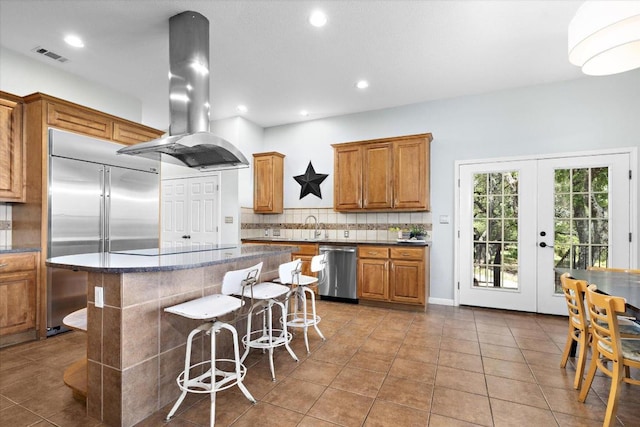 19200 White Horse Cv, Spicewood, TX 78669 - kitchen featuring stainless steel appliances, island range hood, tasteful backsplash, brown cabinets, and tile patterned floors
