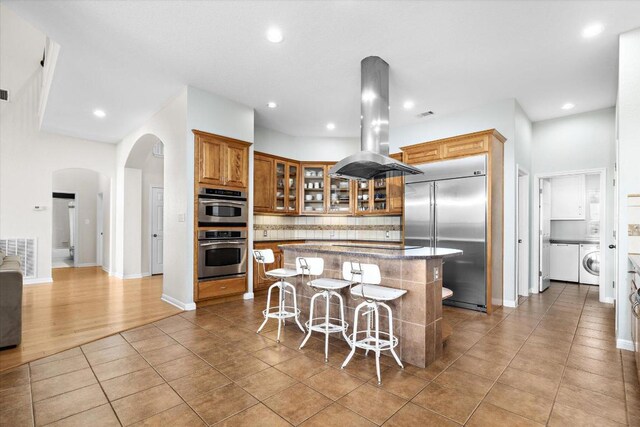 19200 White Horse Cv, Spicewood, TX 78669 - kitchen featuring stainless steel appliances, island range hood, arched walkways, decorative backsplash, and a kitchen island