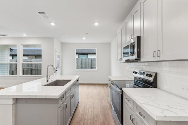 kitchen featuring visible vents, a sink, light wood-style flooring, backsplash, and stainless steel appliances