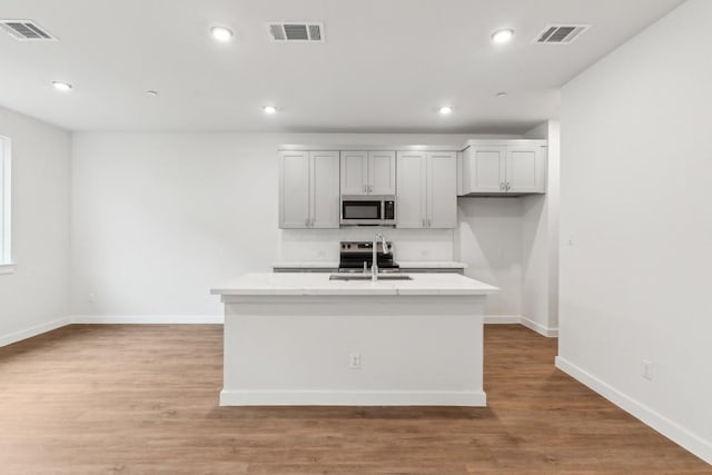kitchen featuring backsplash, stainless steel appliances, visible vents, and a center island with sink