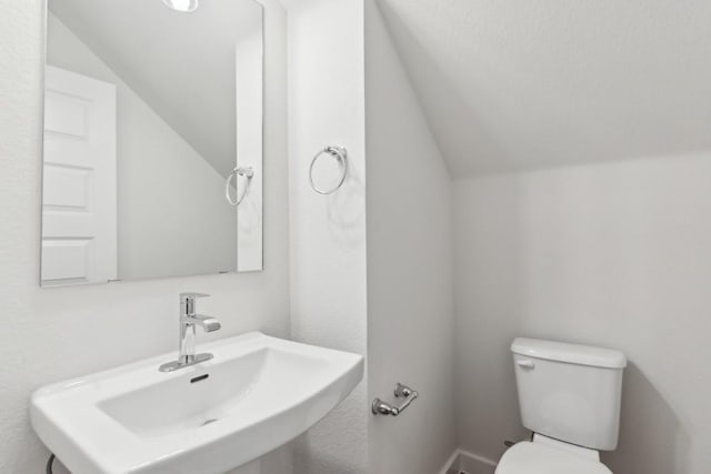 half bathroom featuring toilet, a sink, and lofted ceiling