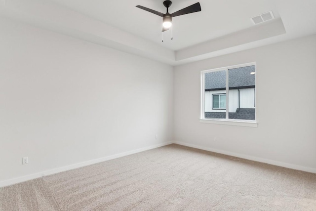 spare room featuring carpet flooring, a tray ceiling, visible vents, and ceiling fan